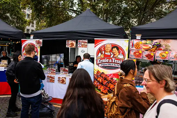Gäste vor einem Grillstand, auf den Plakaten BBQ-Spieße und Siopao