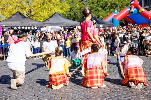 Tinikling von hinten gesehen: die Bambusträger knien, eine Tänzerin springt