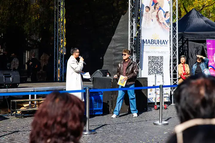 Moderation vor der Bühne, der Gast hält eine gelbe Quizkarte