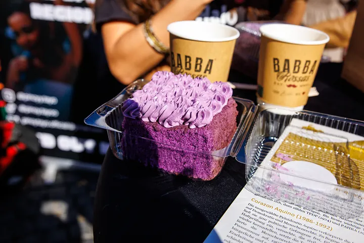 Ube Cake mit Sahnetupfen, dahinter zwei Kaffeebecher
