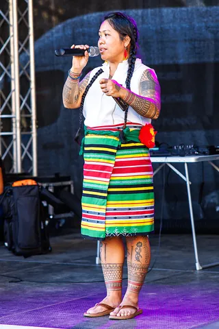 Rednerin mit traditionellen Tattoos und gestreiftem Wickelrock auf der Bühne