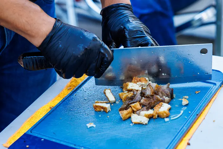 Ein Koch hackt gebratenes Fleisch mit dem Hackmesser